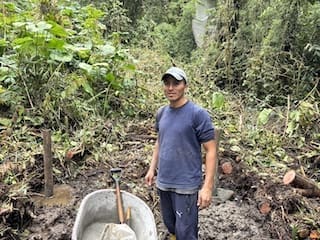 Byron standing in a muddy clearing with a wheelbarrow and shovel, working on a bird observation platform in the forest at Cabañas Tamiaju.